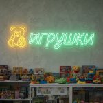 Неоновая вывеска «ИГРУШКИ» с изображением медвежонка и зелёно-жёлтой подсветкой