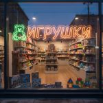Неоновая вывеска «ИГРУШКИ» с зелёно-оранжевой подсветкой и изображением медвежонка