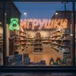 Неоновая вывеска «ИГРУШКИ» с зелёно-оранжевой подсветкой и изображением медвежонка